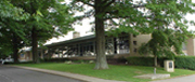 A view of a modern building surrounded by green trees and grass, with a pathway leading up to it.