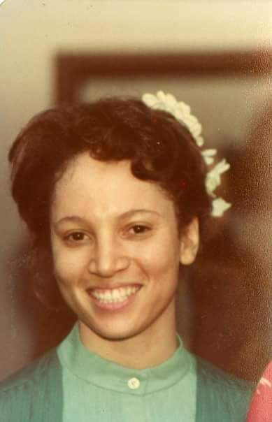 A woman with a flower in her hair smiles warmly at the camera, exuding joy and confidence.