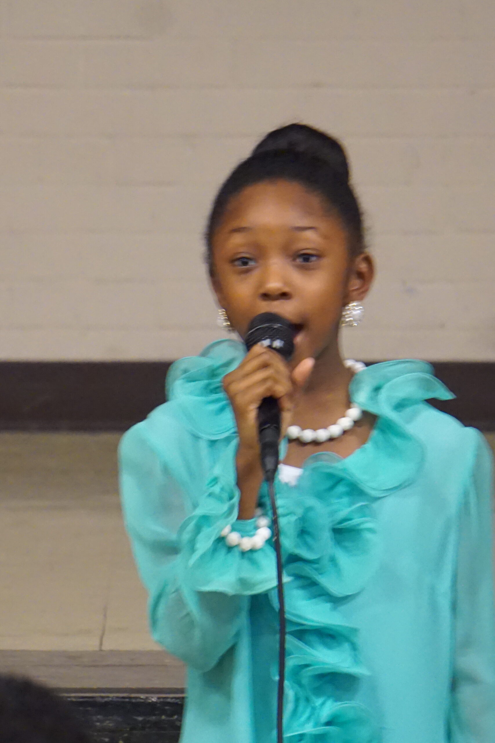 A young girl in a blue dress passionately singing into a microphone on stage.