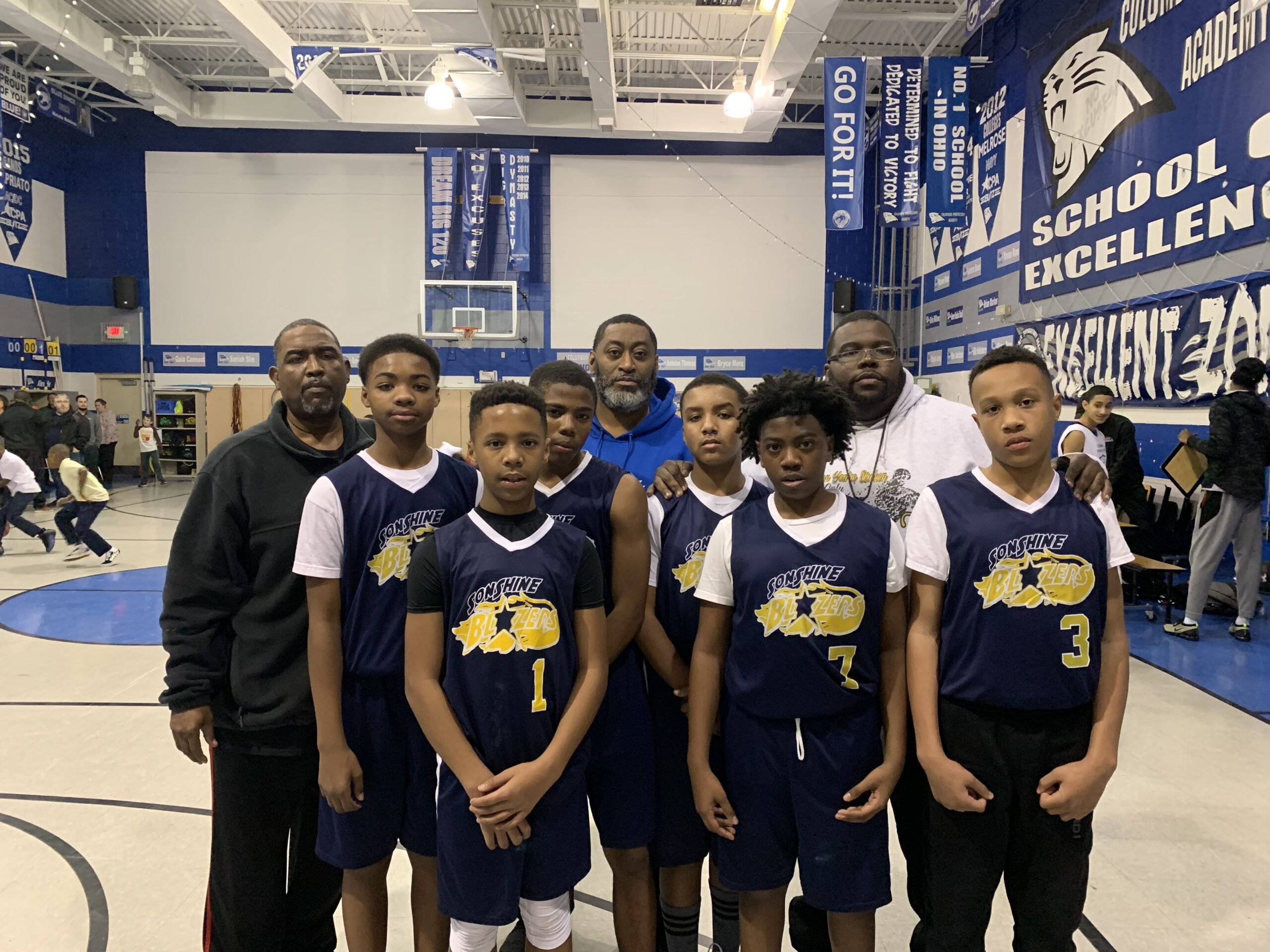 A group of boys in basketball uniforms standing together, smiling and posing for a team photo on a court.