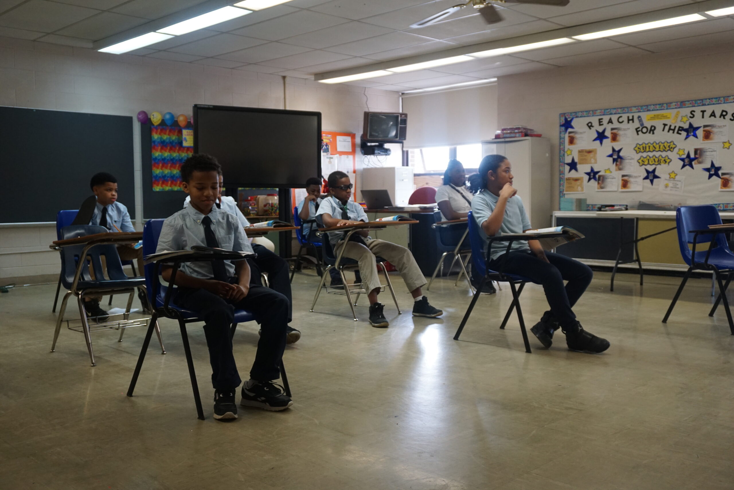 A classroom filled with children seated at desks, engaged in learning activities and interacting with each other.