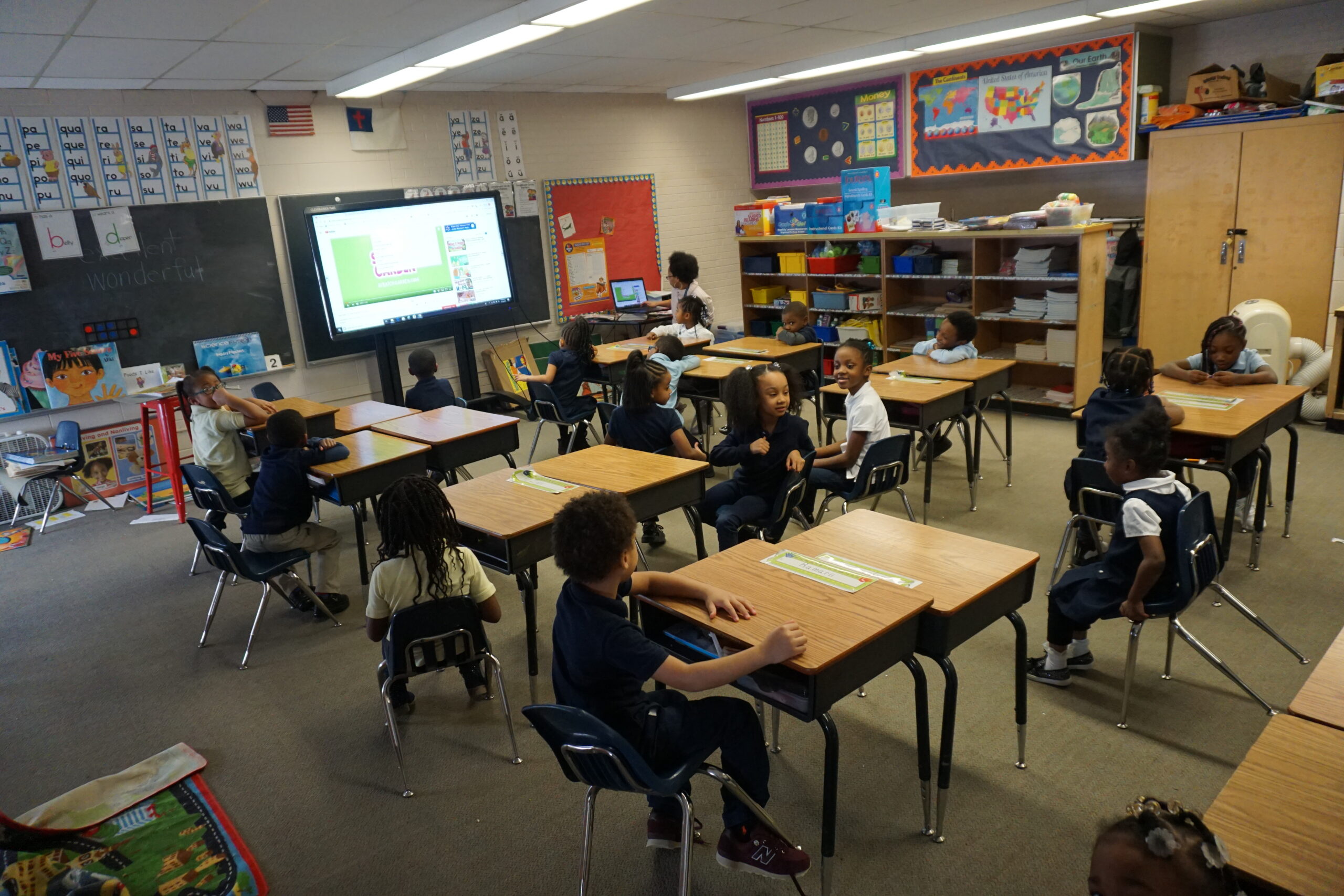 A classroom filled with children seated at desks, engaged in learning activities and interacting with each other.
