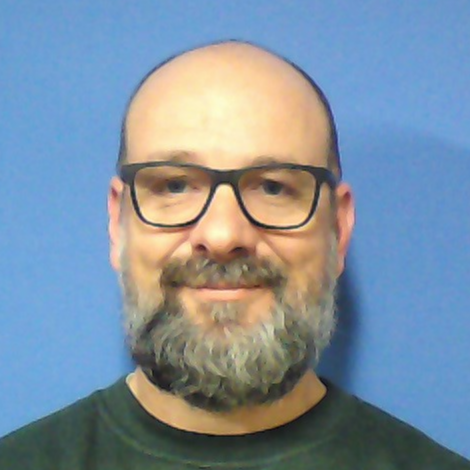Bald man wearing glasses, green shirt, against a blue background