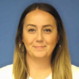 A woman with long, straight hair and hoop earrings smiles at the camera against a blue background.