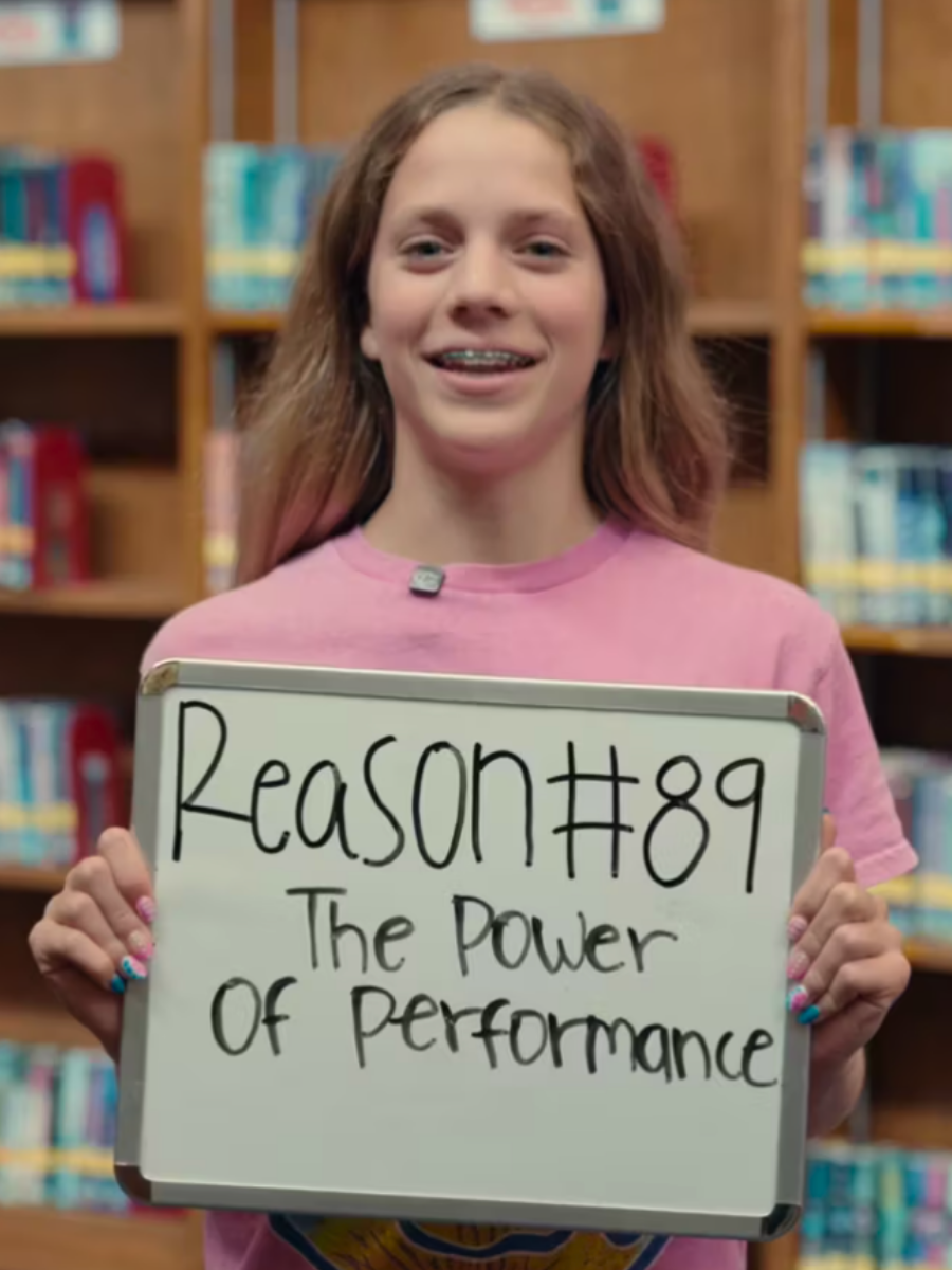 Female student holding sign that says Reason #89 The Power of Performance