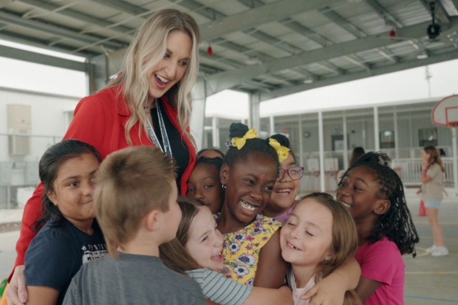 Teacher with many kids hugging her on a basketball court