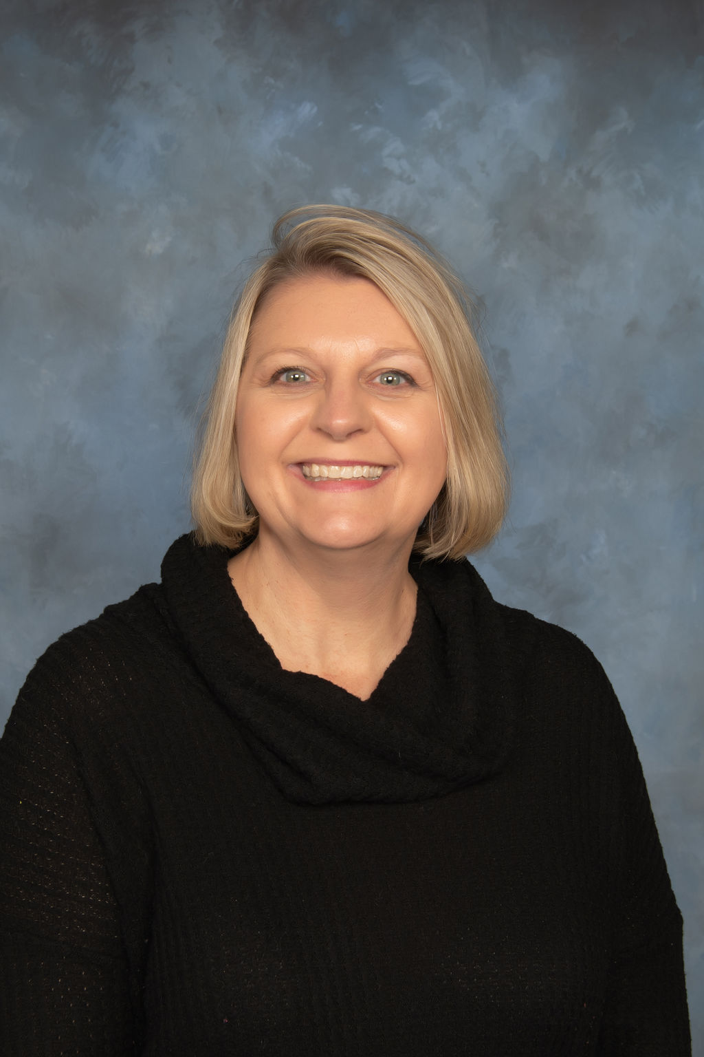 A woman wearing a black sweater smiles warmly at the camera, exuding a friendly and approachable demeanor.