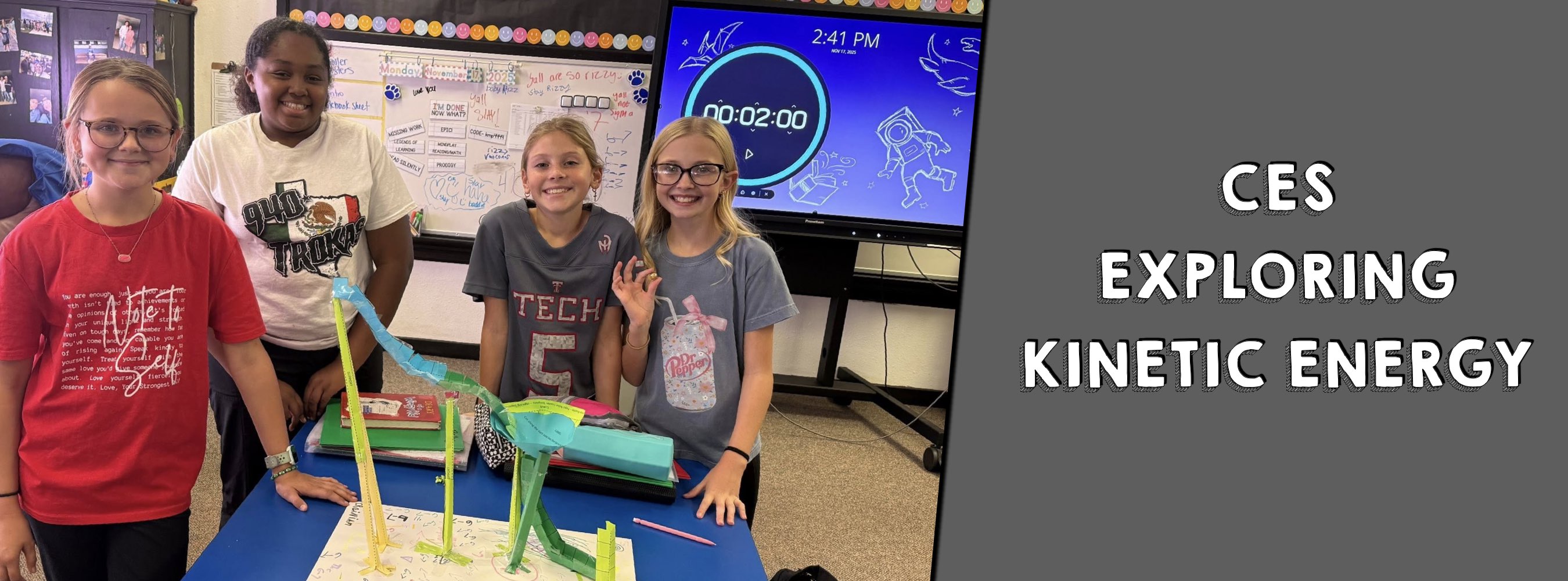 Four smiling children stand around a blue table with a kinetic energy project using colorful tubes. A screen displays a timer. Text reads, "CES Exploring Kinetic Energy."