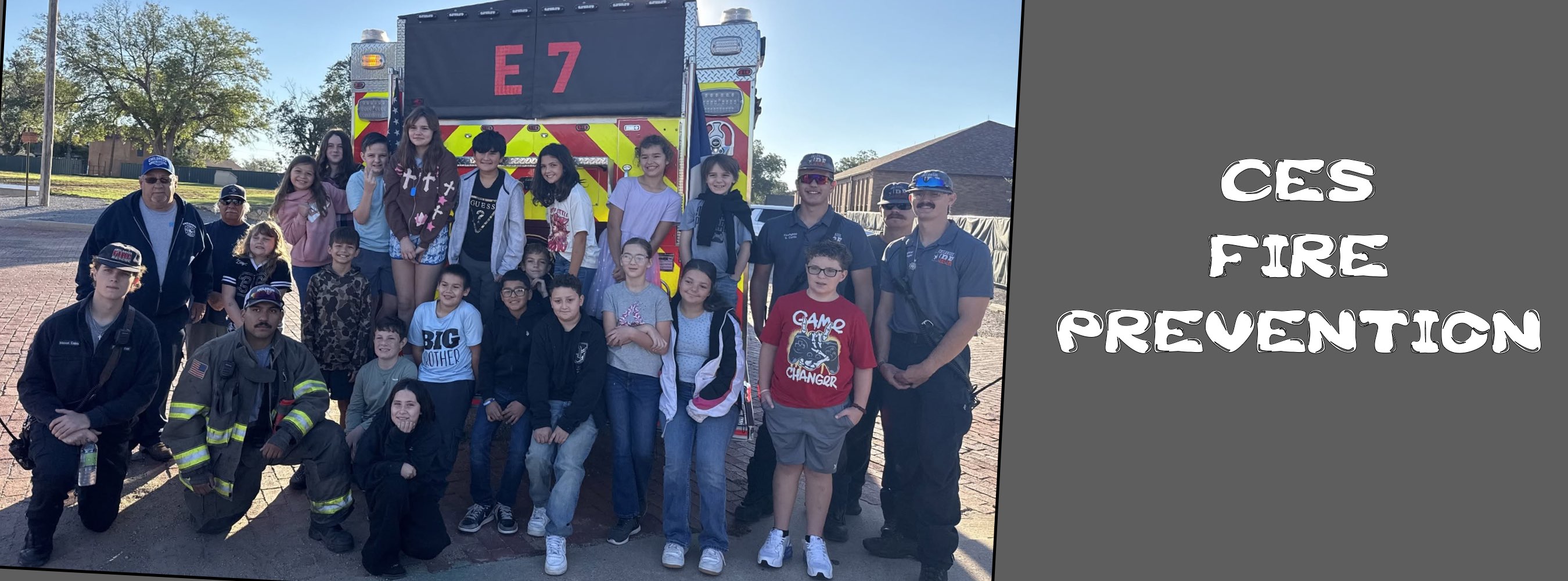 A cheerful group of firefighters and community members poses beside an E7 fire engine at a CES Fire Prevention event on a sunny day.