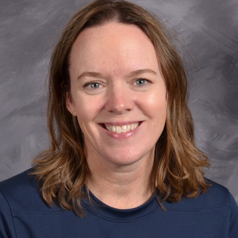 A smiling woman with shoulder length dark hair, wearing a navy blue shirt, gray background.