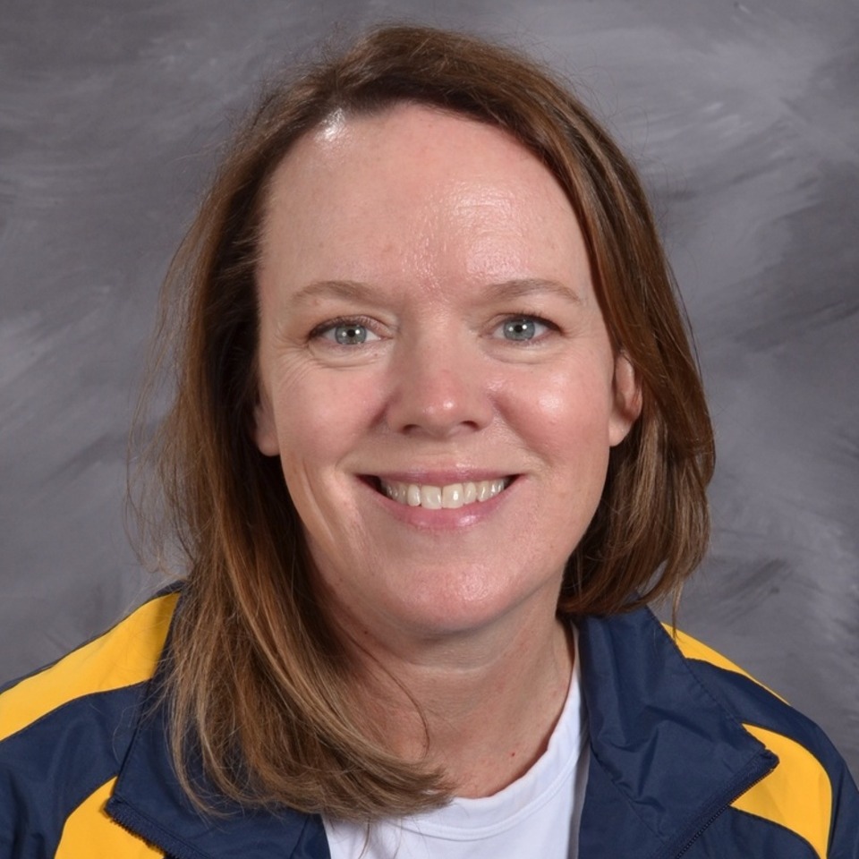 A smiling woman with shoulder length dark hair, wearing a navy blue and yellow shirt, gray background.
