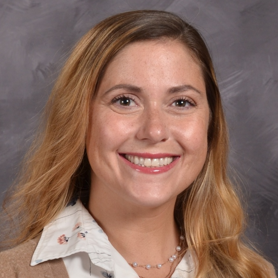 Women with sandy long blond hair wearing a white and tan shirt, grey background