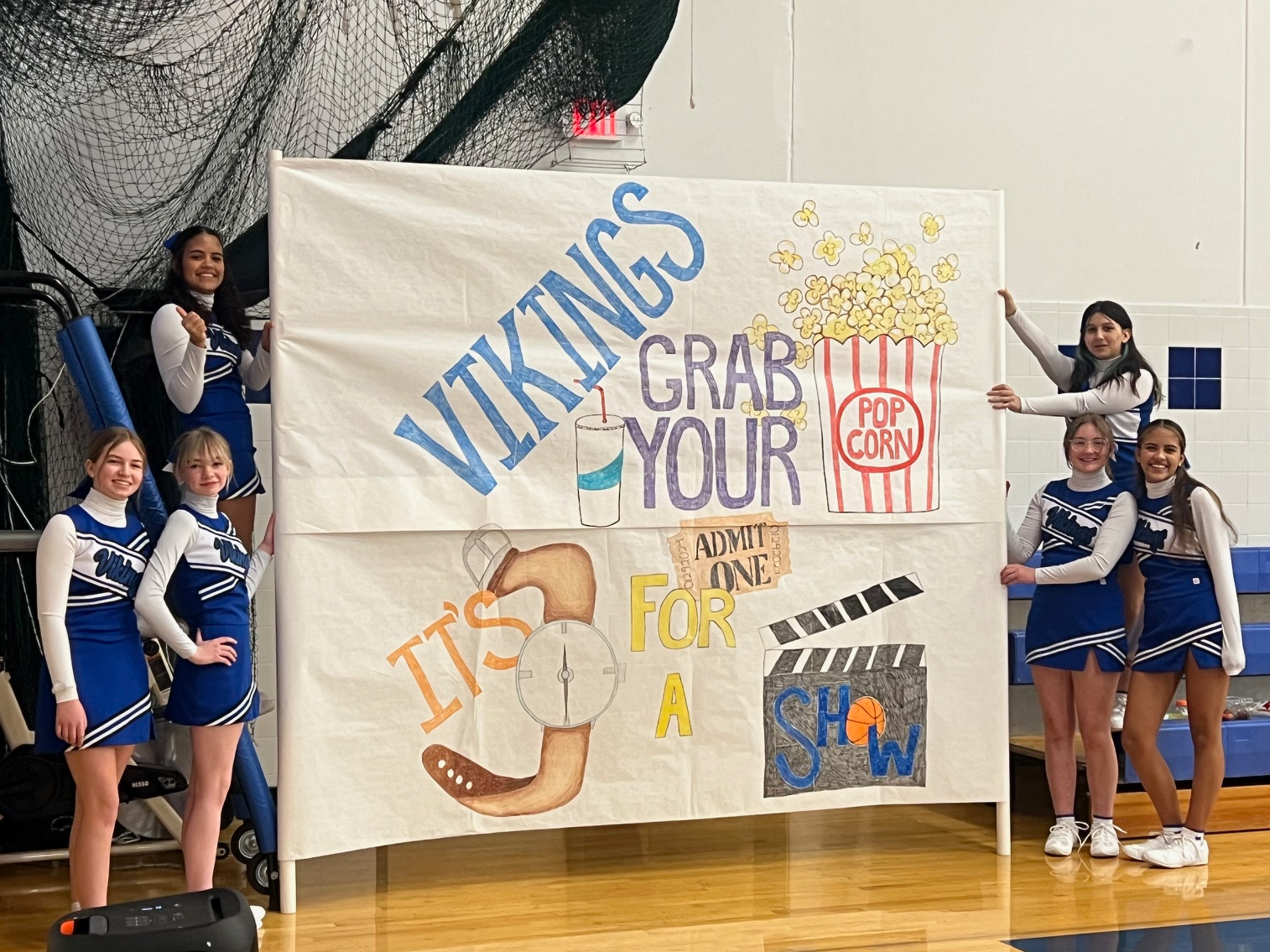 Cheerleaders with large poster for team to run through. 