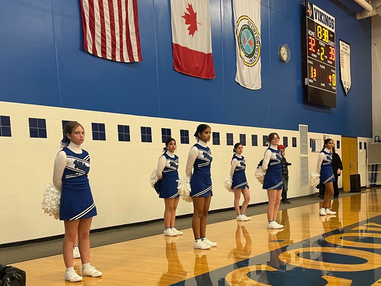 Cheerleaders standing at basketball game in the gym. 