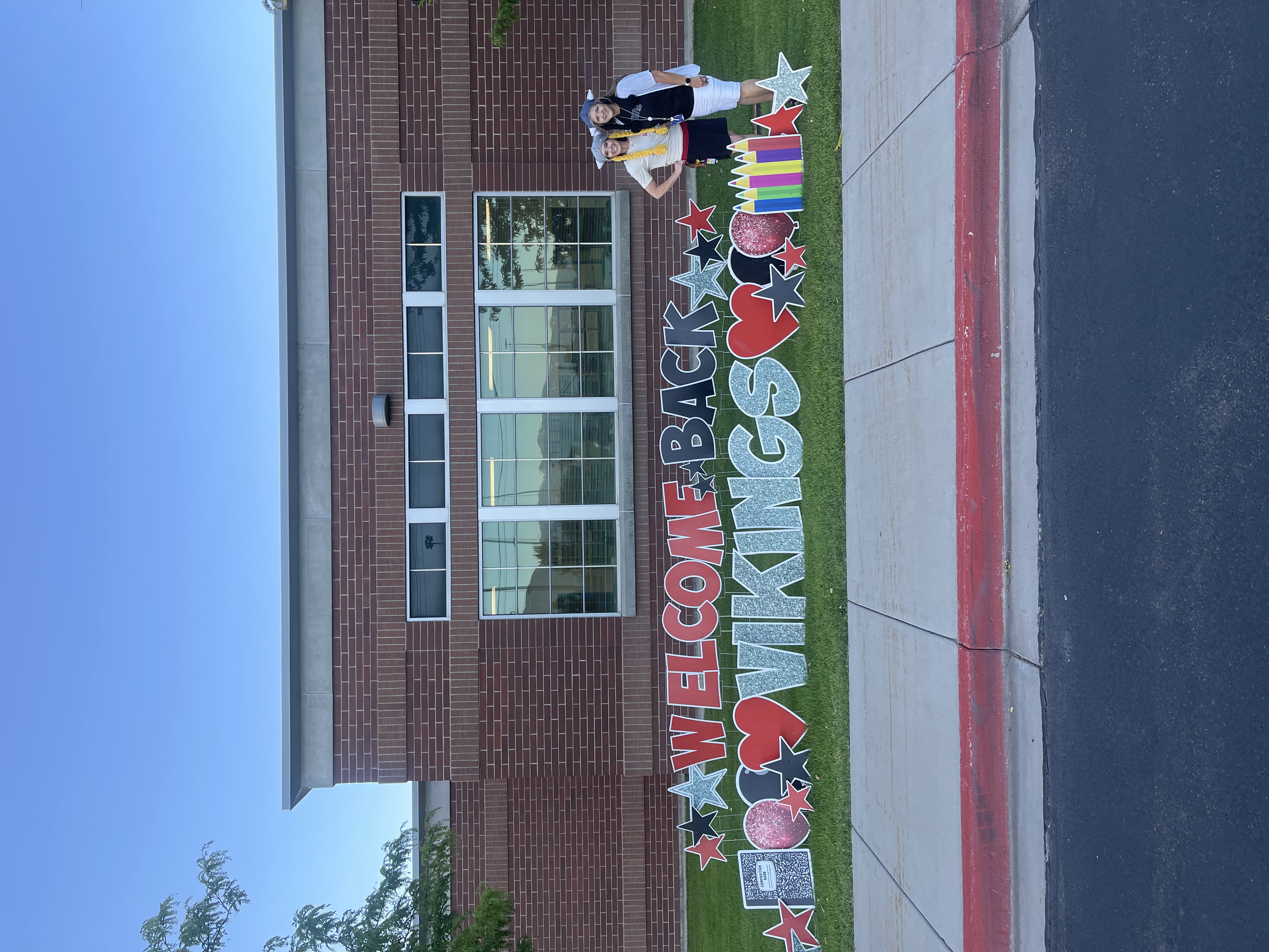 Welcome back Vikings yard sign with the principal and assistant principal wearing viking hats standing outside the school