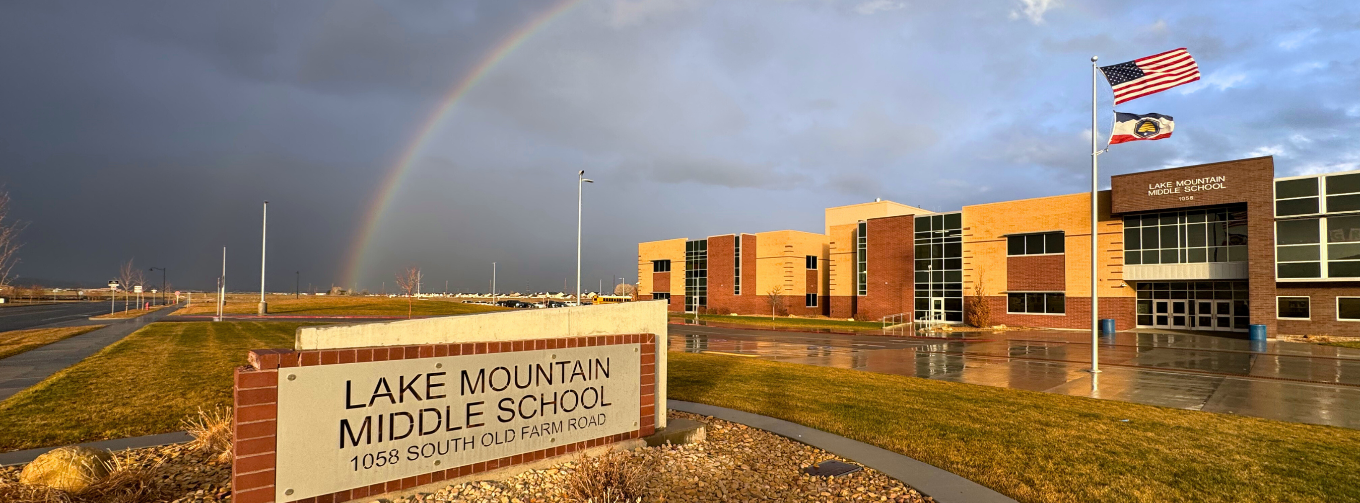 A photo of the front of Lake Mountain Middle School showing the road sign, a stormy sky, and a rainbow over the school.