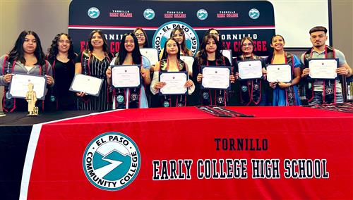 Students proudly display their certificates in front of a table, celebrating their achievements together.