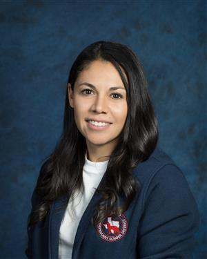 A woman wearing a blue jacket over a white shirt, standing confidently with a neutral expression.