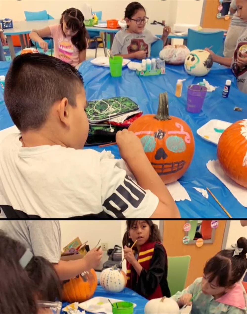 Children are engaged in a pumpkin painting activity at a table, with various painted pumpkins and art supplies visible.