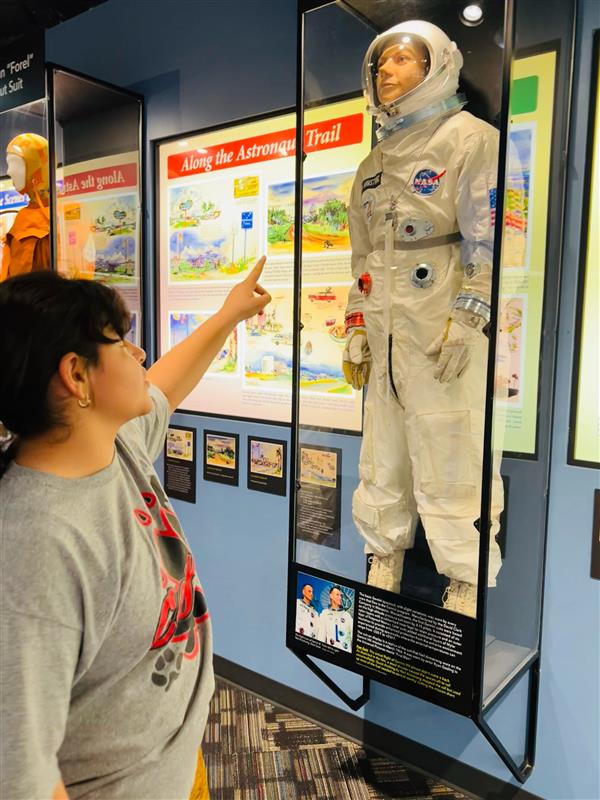 A person points at a display featuring an astronaut suit in a museum, surrounded by educational panels about space exploration.