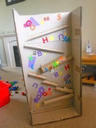 A cardboard structure with slanted tubes and colorful letters attached to its surface, designed as a playful educational toy for children.