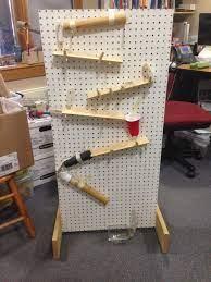 A vertical pegboard with wooden ramps and a red cup at the bottom, designed to demonstrate a marble run or similar kinetic activity.