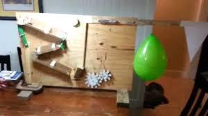 A wooden marble run structure featuring ramps and obstacles, with a green balloon and a snowflake decoration, set on a table in a room.