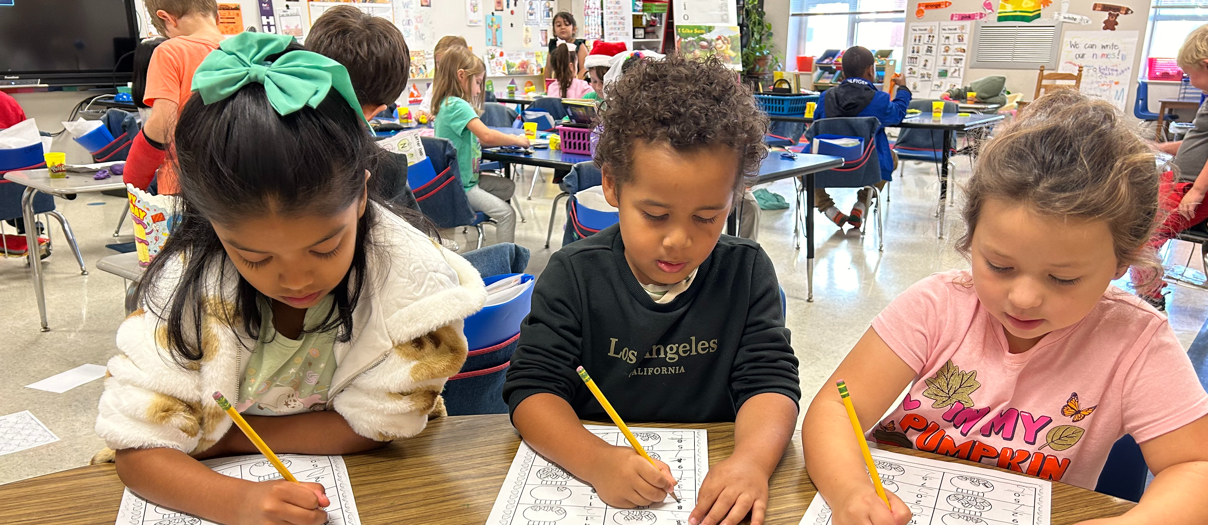 three children writing on paper in the classroom