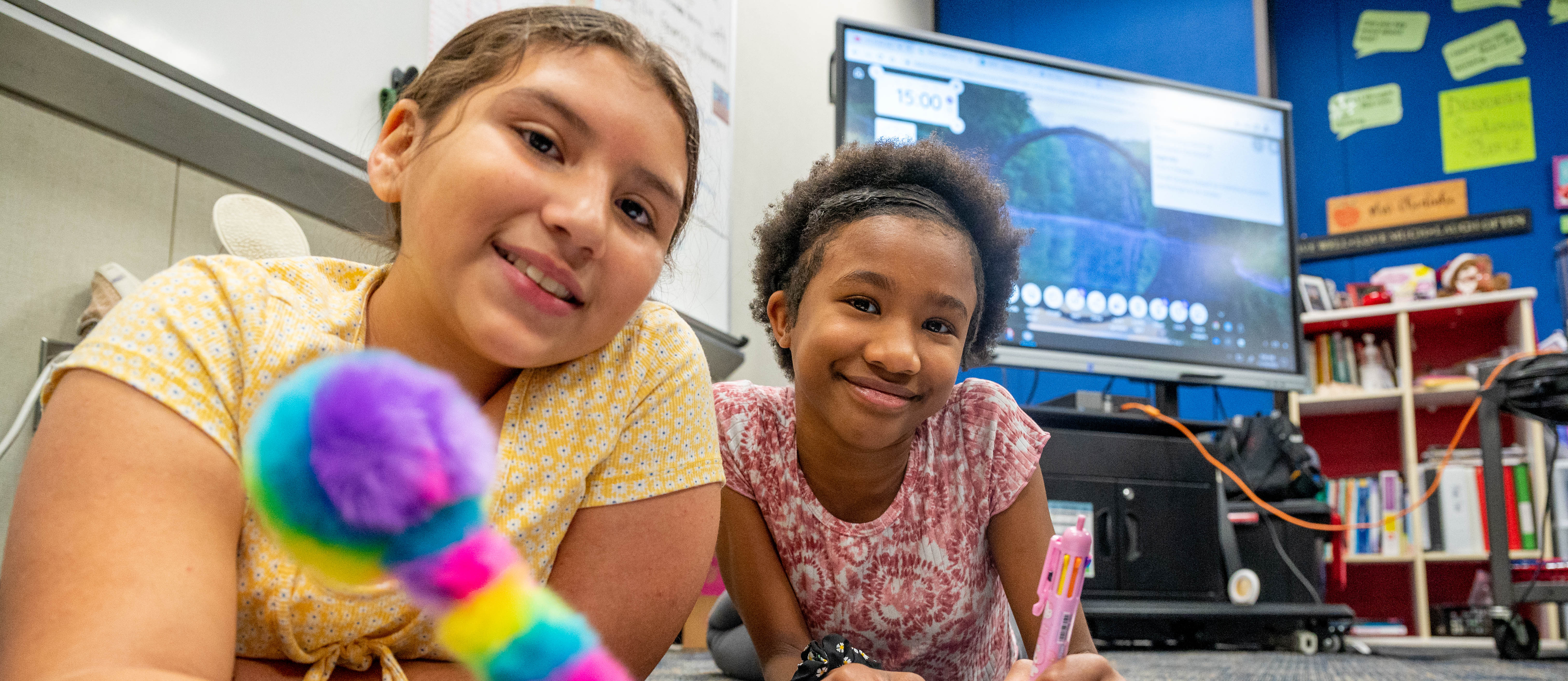 Two students smiling at the camera while working on an assignment