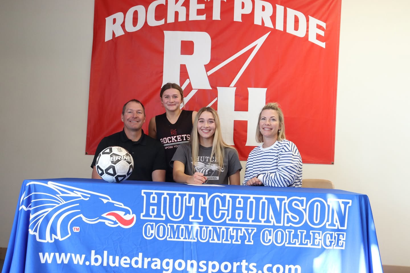 Ella signing her commitment surrounded by family.