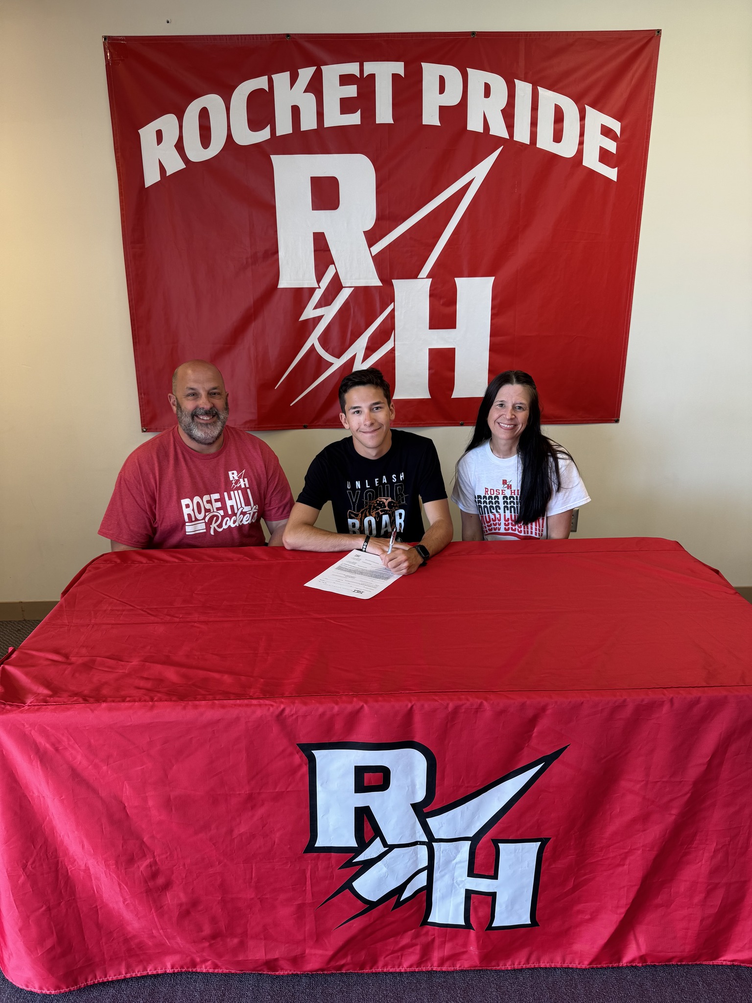 Samuel signs his commitment surrounded by his parents.