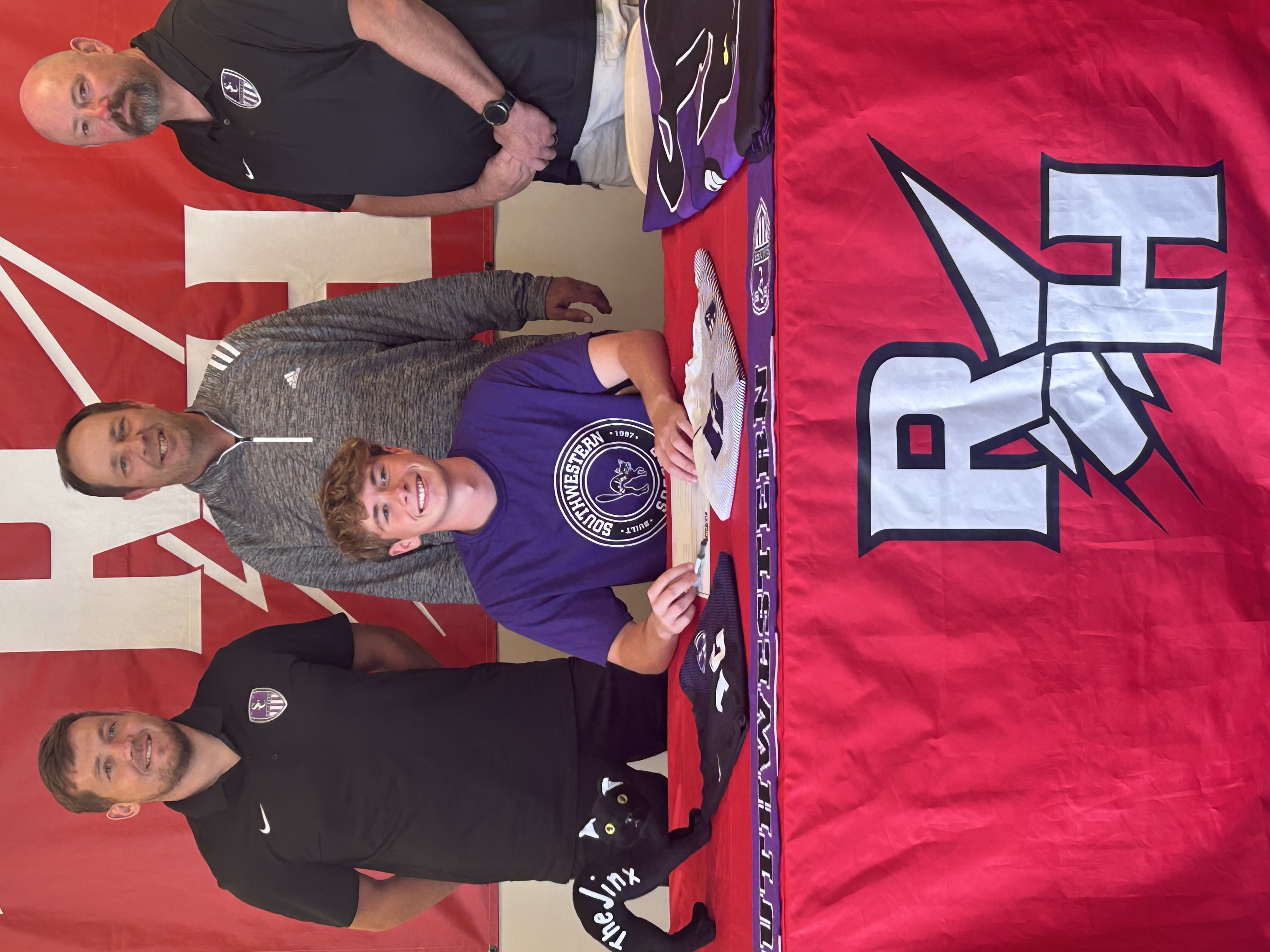 Luke signs his commitment surrounded by coaches.