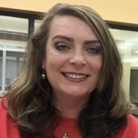 A woman in a red shirt labeled "librarian" smiles while standing in a library filled with books.
