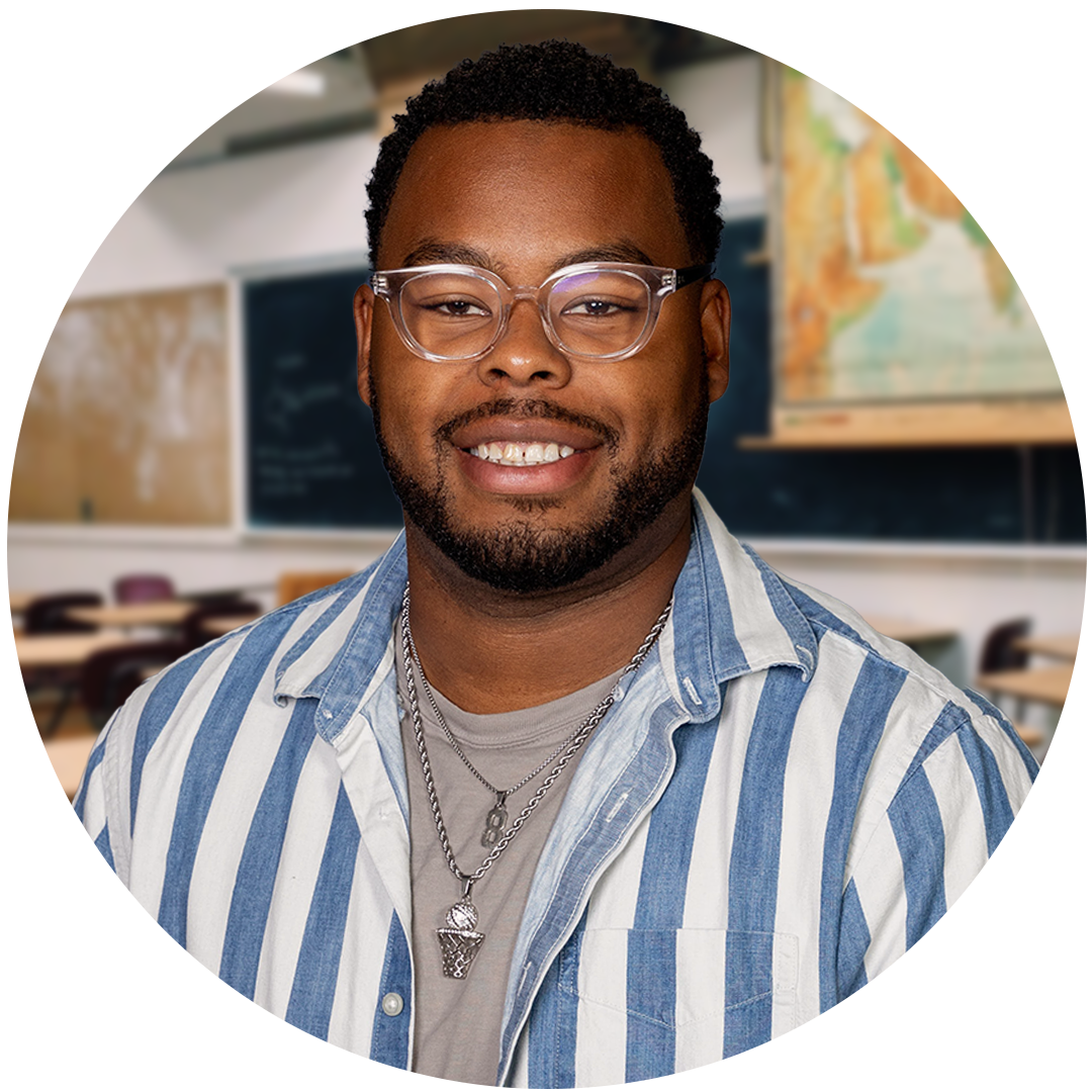 A smiling man with glasses and a striped shirt stands in front of a classroom setting, featuring chalkboards and desks in the background.