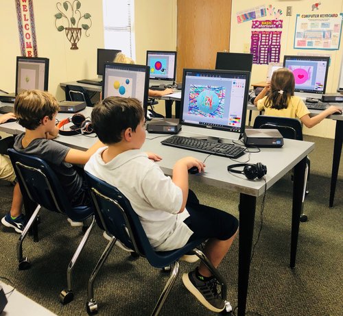 A classroom setting with several children seated at computers, focused on their screens while working on projects.