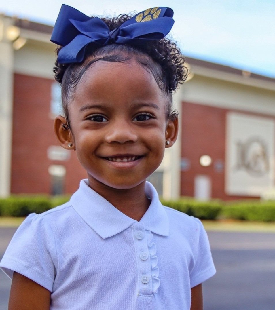 Girl wearing a bow and standing in front of a school