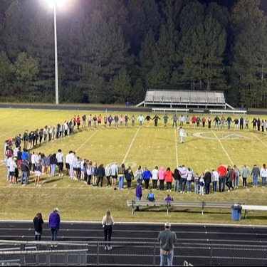large circle of students praying on football field