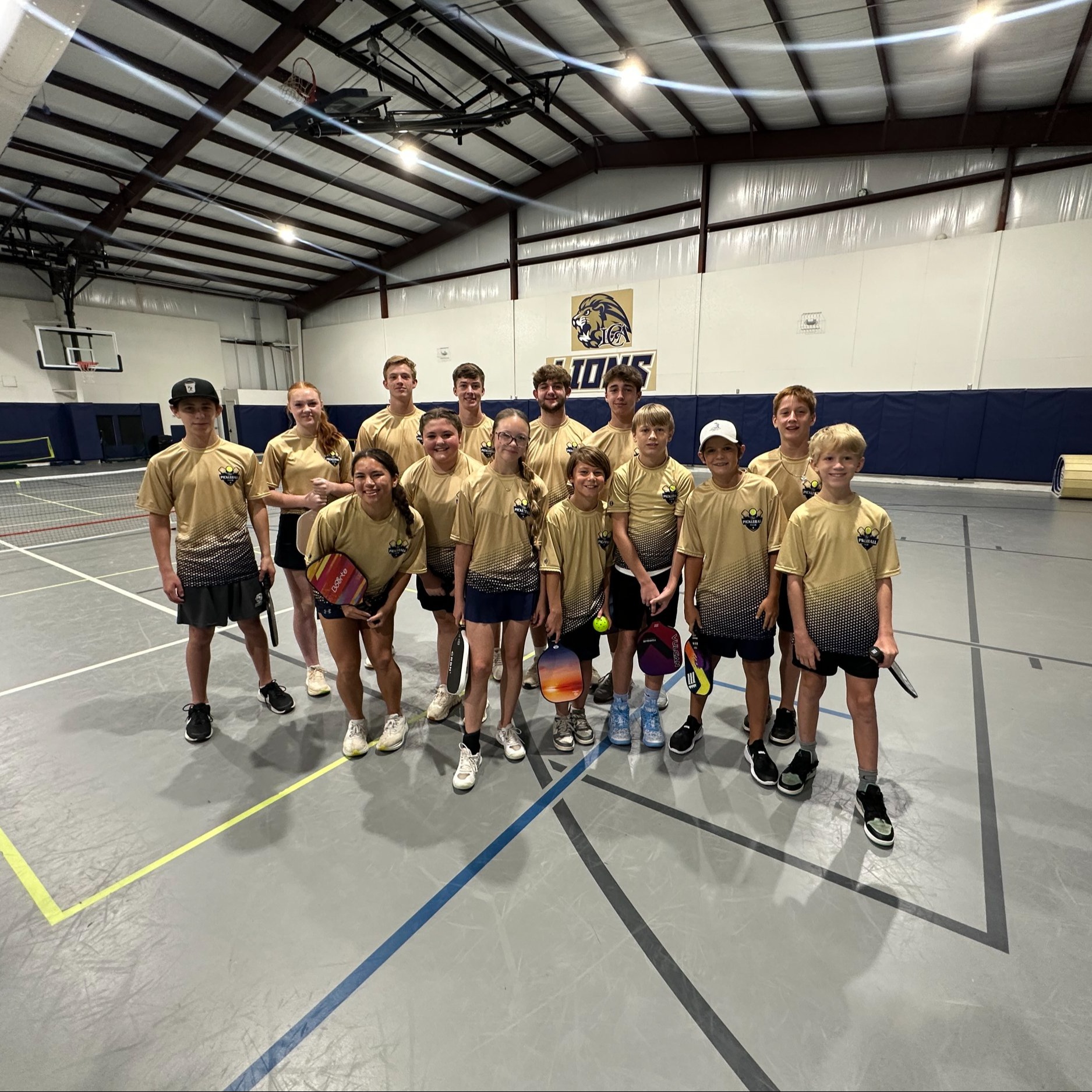 group of students in matching shirts standing in gym and smiling