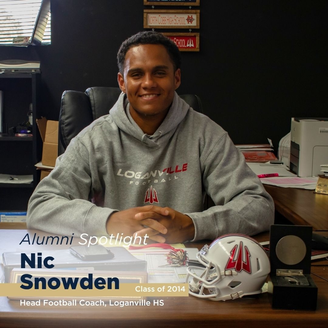 A smiling young man with curly hair and a beard stands outdoors, wearing a green shirt with 'RUF' printed on it, with trees and water in the background.