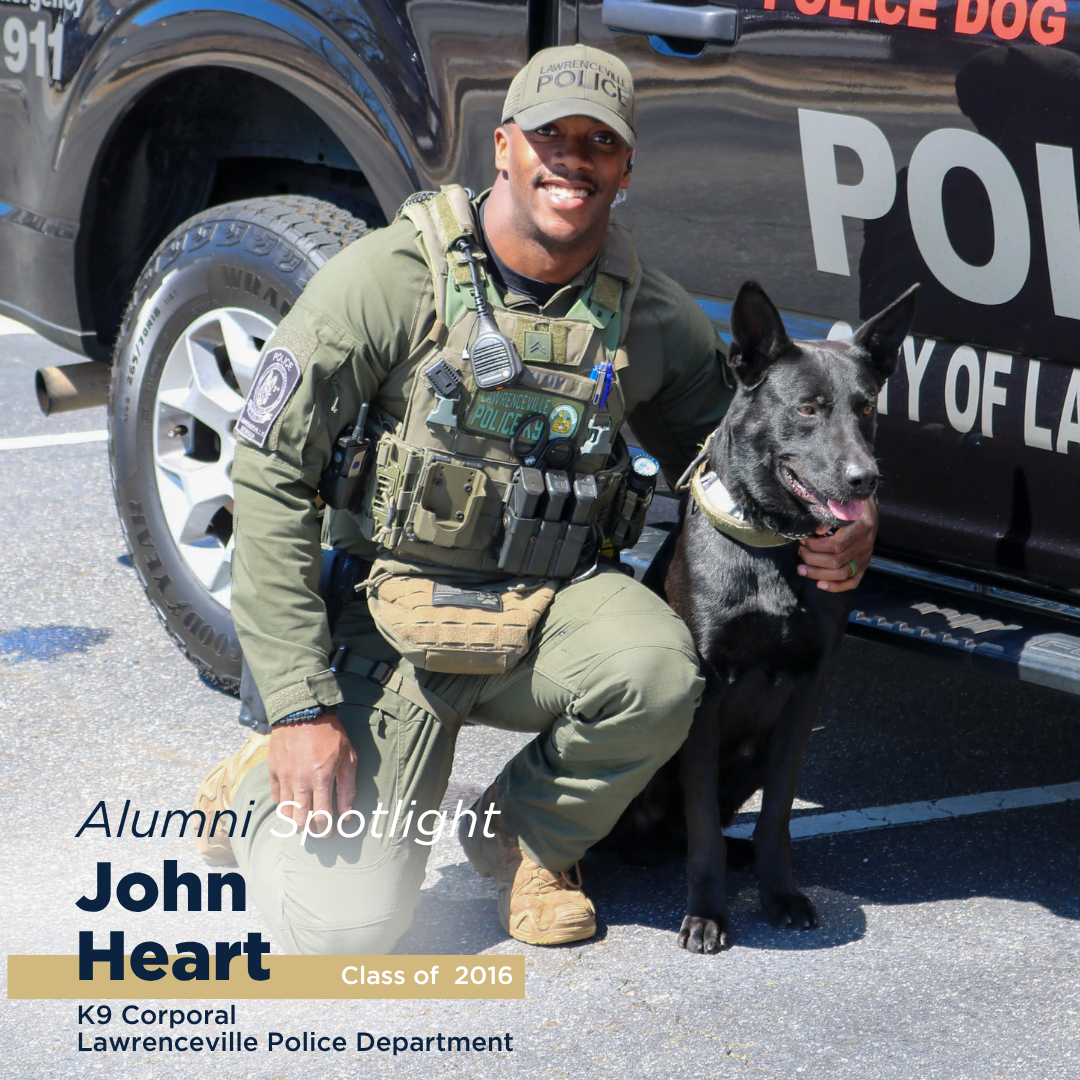 A policeman poses for a photo smiling with his K9 dog, featuring him an alumni spotlight blog post.