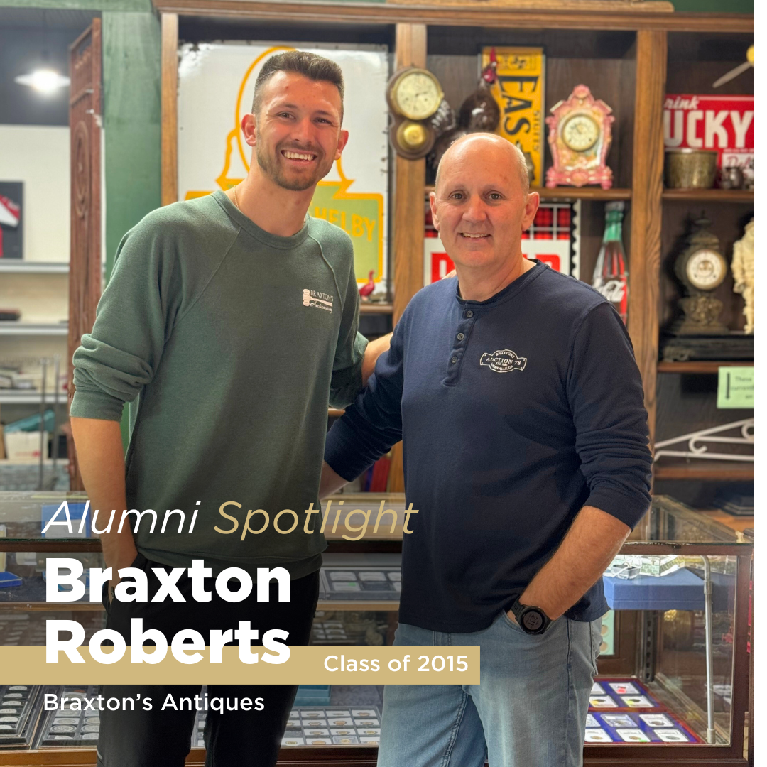 A black haired man poses for a photo next to an older bald man in a shop while being featured in an alumni spotlight series.