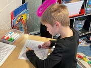 A boy focused on solving a math problem at his desk in a classroom setting.