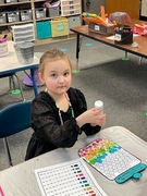 A young girl sits at a table, focused on coloring in her coloring book with vibrant crayons scattered around her.