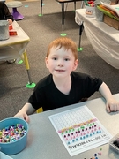 A young boy sits at a table, focused on a number chart in front of him, engaged in learning activities.