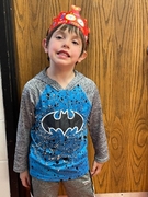 A young boy wearing a Batman shirt and hat, smiling while standing outdoors.