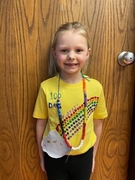 A young girl in a yellow shirt and necklace smiles brightly, showcasing her cheerful personality.