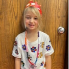 A young girl with a floral shirt and a headband smiles, showcasing her playful and cheerful personality.