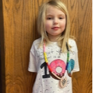 A young girl smiles while wearing a shirt featuring a colorful donut graphic.