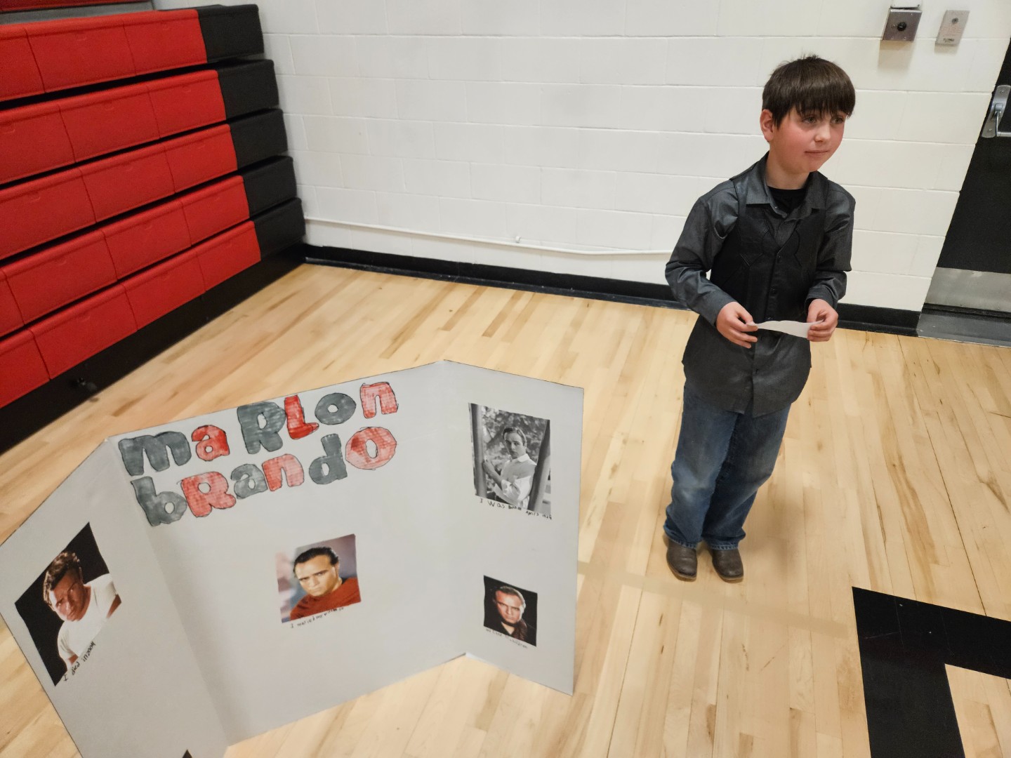 A boy stands in front of a display board showcasing various pictures, engaging with the visual content.