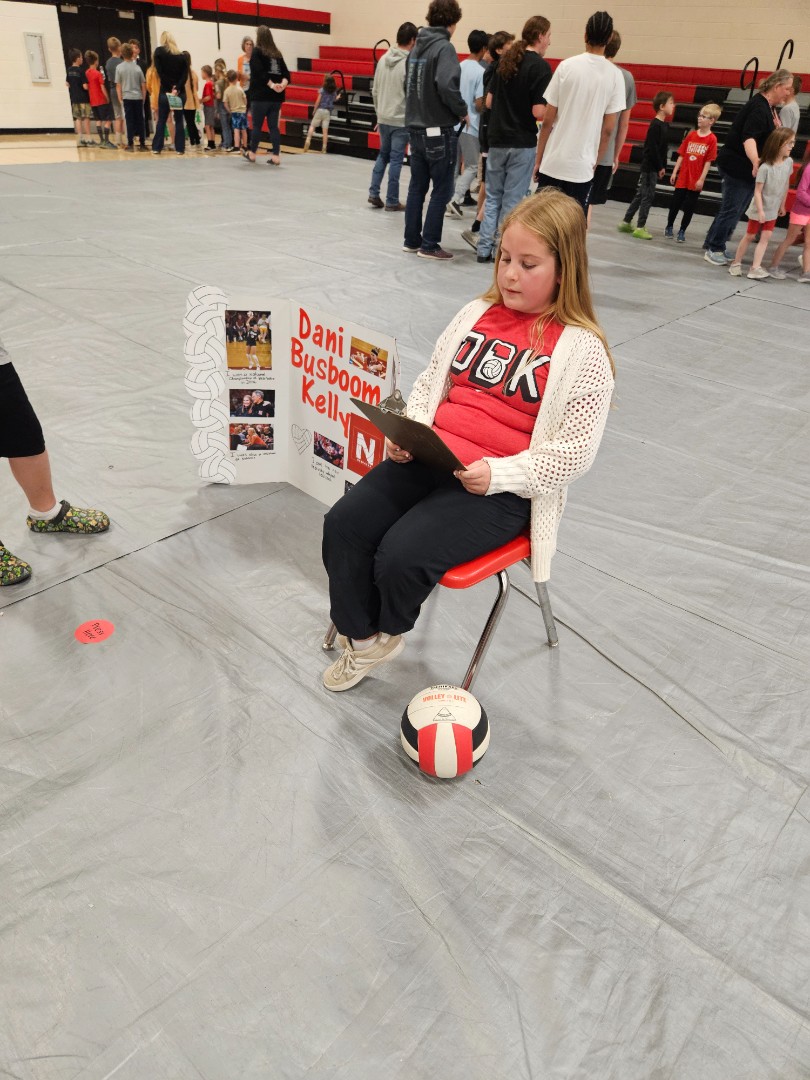 A girl sitting on a chair, holding a volleyball, with a focused expression on her face.